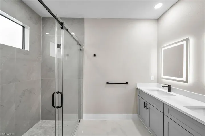 Bathroom with double vanity, a marble finish shower, and light marble finish floors
