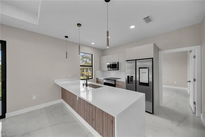 Kitchen with light marble finish floors, appliances with stainless steel finishes, a peninsula, modern cabinets, and recessed lighting