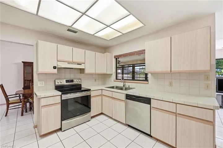 Kitchen with light brown cabinetry, appliances with stainless steel finishes, tile countertops, and backsplash