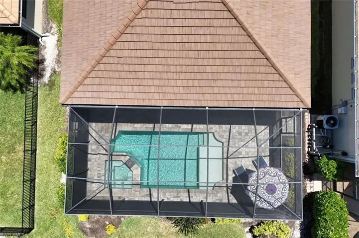 Screened pool enclosure featuring a rectangular swimming pool with integrated spa, paver decking, and a terracotta tile roofline