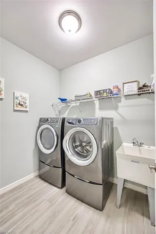 Dedicated laundry area featuring wood-finish flooring, a utility sink, and wall-mounted shelving