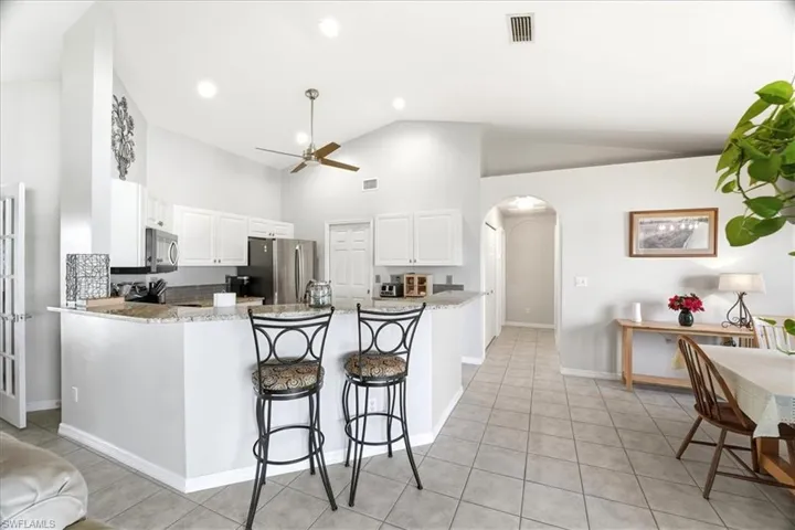 Kitchen with a breakfast bar area, arched walkways, white cabinets, ceiling fan, and high vaulted ceiling