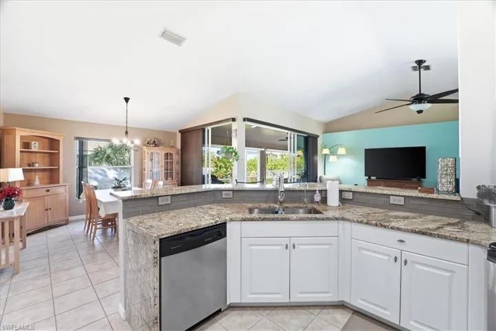 Kitchen featuring stainless steel dishwasher, lofted ceiling, light stone counters, and healthy amount of natural light
