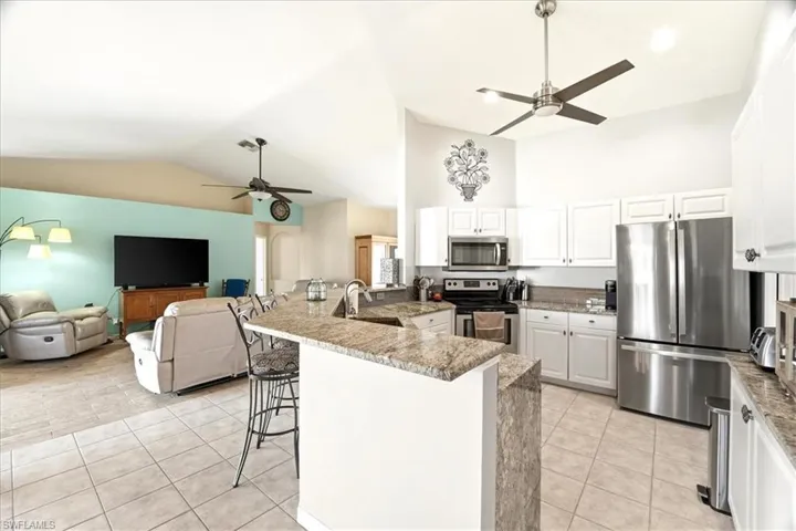 Kitchen featuring a ceiling fan, white cabinetry, stainless steel appliances, light tile patterned floors, and high vaulted ceiling
