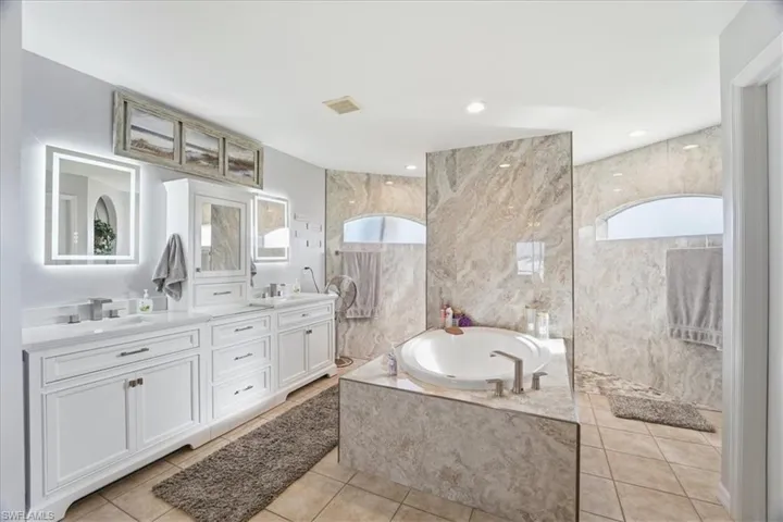 Full bath with double vanity, a garden tub, a marble finish shower, and tile walls
