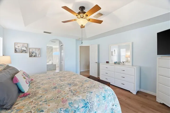 Bedroom with a tray ceiling, light wood-type flooring, arched walkways, and a ceiling fan