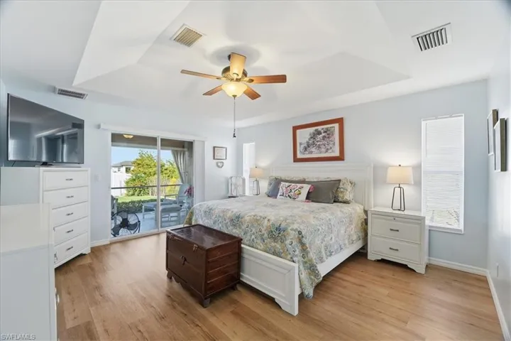 Bedroom featuring a tray ceiling, light wood finished floors, access to outside, and a ceiling fan