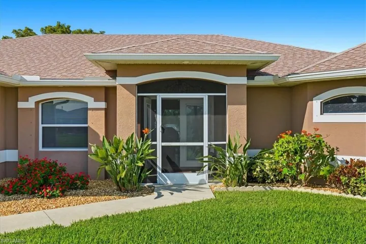 Doorway to property featuring stucco siding, roof with shingles, a yard, and a sunroom