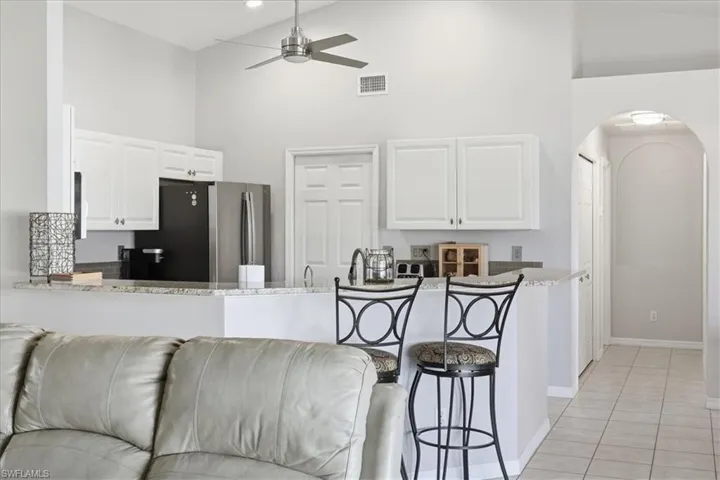 Kitchen featuring a high ceiling, white cabinets, a breakfast bar, arched walkways, and light stone counters