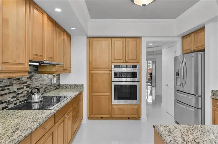Kitchen with tasteful backsplash, appliances with stainless steel finishes, recessed lighting, ornamental molding, and light stone counters