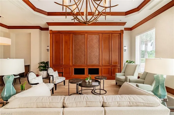 Living room with light wood finished floors, a raised ceiling, ornamental molding, and a chandelier