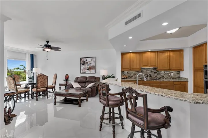 Kitchen with crown molding, tasteful backsplash, light stone countertops, a breakfast bar area, and brown cabinets