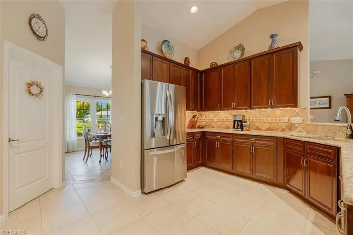 Kitchen with stainless steel refrigerator with ice dispenser, light stone counters, light tile flooring, tasteful backsplash, and lofted ceiling