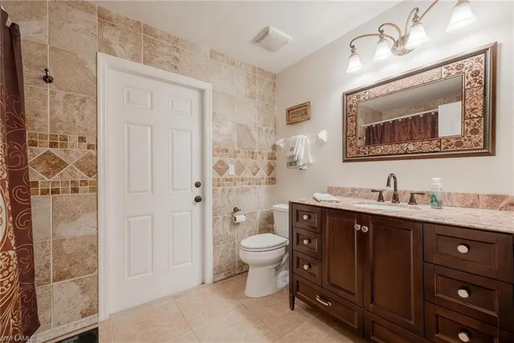 Bathroom with tile floors, tile walls, toilet, and vanity