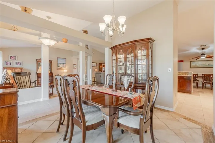Dining area featuring ceiling fan with notable chandelier, light tile floors, and lofted ceiling