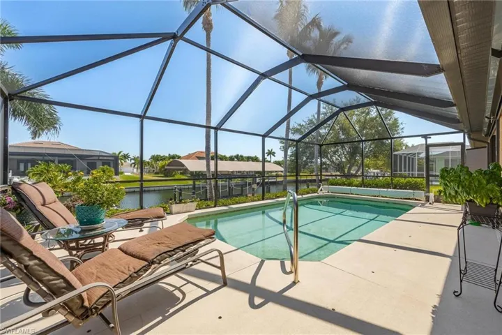 View of swimming pool with a patio area, glass enclosure, and a water view