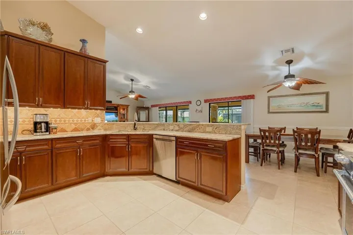 Kitchen featuring kitchen peninsula, ceiling fan, light stone countertops, stainless steel dishwasher, and light tile floors