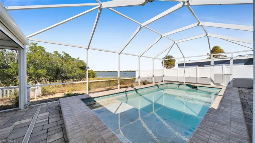 View of swimming pool featuring a water view, glass enclosure, a sunroom, and patio surround