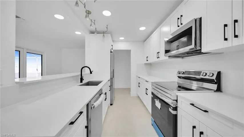 Kitchen featuring stainless steel appliances, recessed lighting, white cabinets, and light stone counters