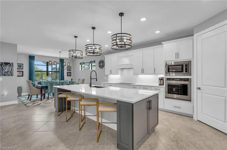 Kitchen with stainless steel appliances, an oversized island with granite sink and grey cabinets, decorative light fixtures, white cabinets, and a breakfast bar area