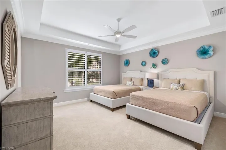 Guest Bedroom 2 featuring a tray ceiling, a ceiling fan, and plantation shutters.