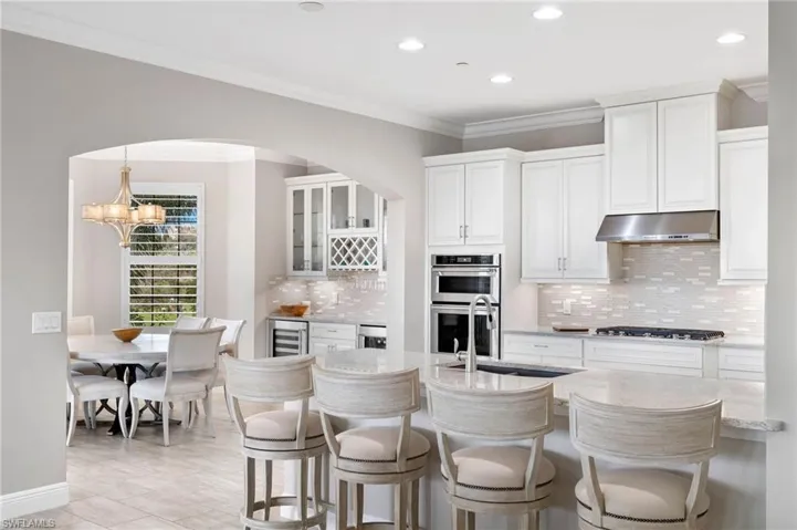 Kitchen featuring crown molding, a breakfast bar, under cabinet lighting, appliances with stainless steel finishes, and wine cooler.
