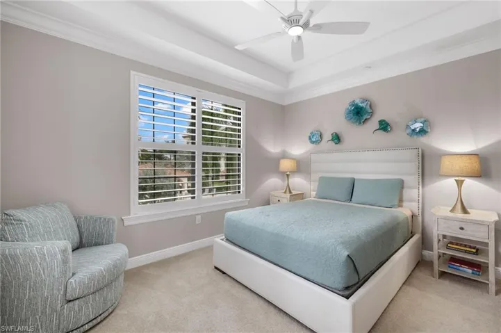 Guest Bedroom 1 featuring crown molding, a tray ceiling, and plantation shutters.