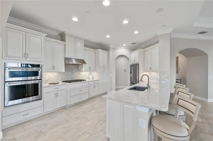 Kitchen with under cabinet lighting, range hood, a kitchen bar, stainless steel appliances, arched walkways, and a natural gas cooktop.