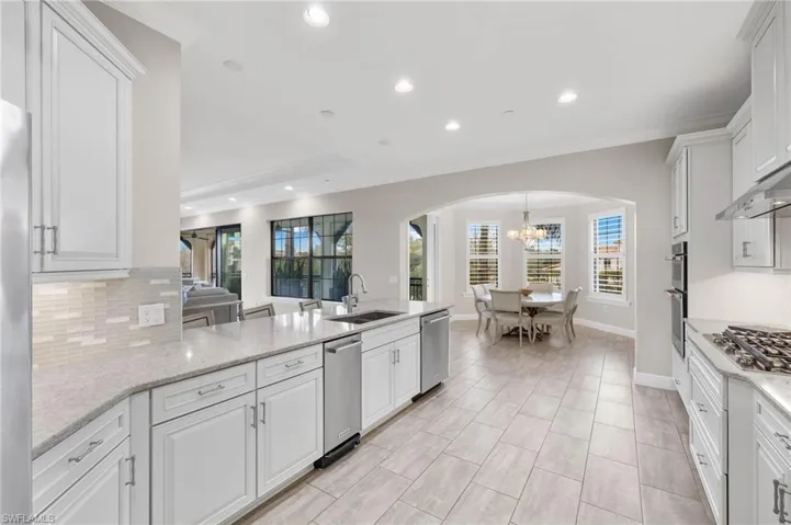 Kitchen featuring arched walkways, appliances with stainless steel finishes, and decorative backsplash.