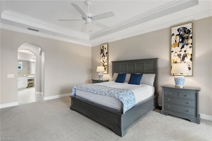 Primary Bedroom featuring crown molding, arched walkways, and a tray ceiling.