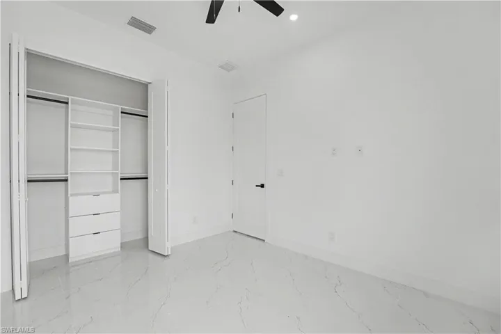 Spacious room featuring a custom closet organization system with shelving and drawers, a flush-mounted ceiling fan, recessed lighting, and large format marble-look tile flooring