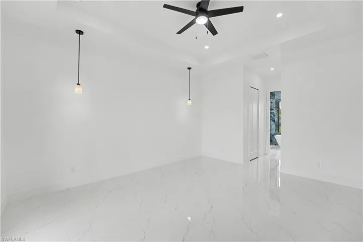 Spacious room featuring white tile flooring, a tray ceiling with recessed lighting, and a contemporary ceiling fan