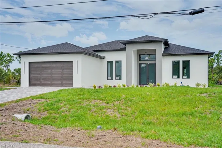 Modern stucco exterior featuring a dark asphalt shingle roof, integrated garage, and a paver driveway