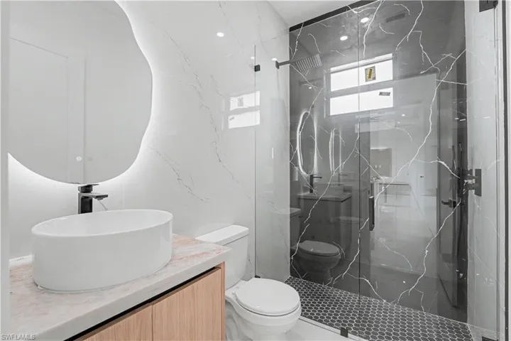 Modern bathroom featuring a custom-shaped illuminated mirror, a vessel sink with a matte black faucet, and a light wood-finish vanity
