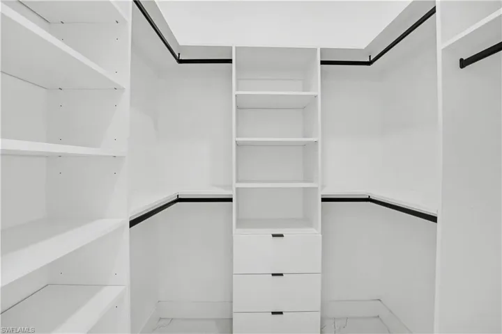 Walk-in closet featuring built-in white cabinetry, multiple shelving units, three integrated drawers, and black hanging rods