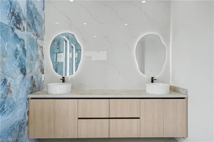 Dual vessel sinks set on a light-toned countertop, complemented by natural wood-finish floating cabinetry