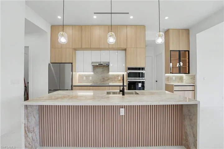 Contemporary kitchen featuring a waterfall island with a slatted wood panel accent, stone countertops, integrated sink with matte black faucet, and stainless steel appliances