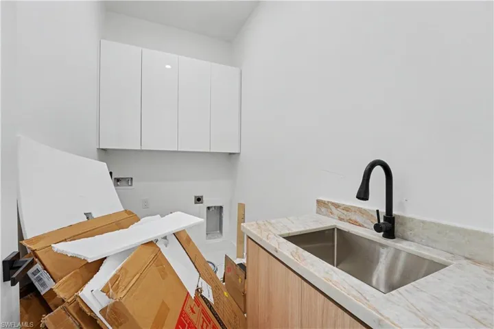 Utility room featuring a stainless steel sink, wood-finish cabinetry, and a black gooseneck faucet