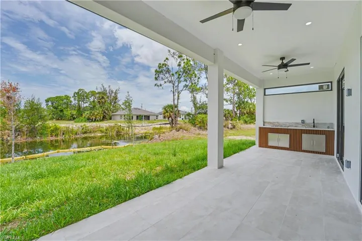 Expansive covered patio featuring light-toned tile flooring, dual ceiling fans, and an outdoor kitchen with a built-in sink, stone-finish countertop, and stainless steel cabinetry