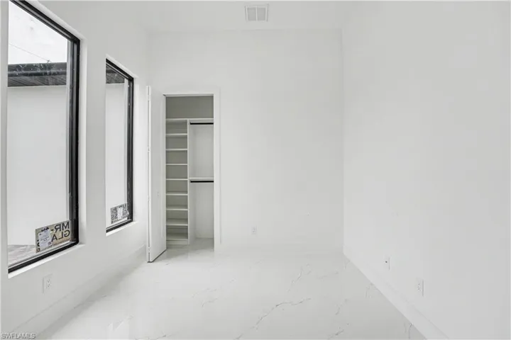 Contemporary room with white walls, a walk-in closet featuring built-in shelving, two tall windows with black frames, and white marble-look flooring