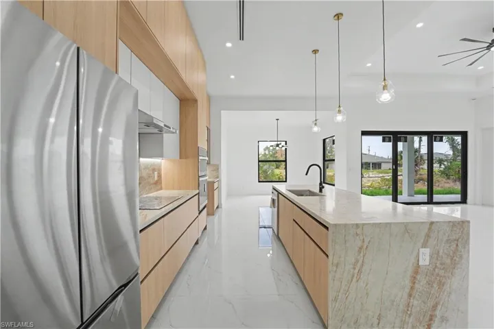Gourmet kitchen featuring a large waterfall island with integrated sink, sleek wood-finish cabinetry, stainless steel appliances, and elegant pendant lighting