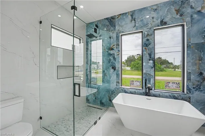 Freestanding soaking tub with a wall-mounted matte black faucet, set against a blue-toned stone-finish accent wall
