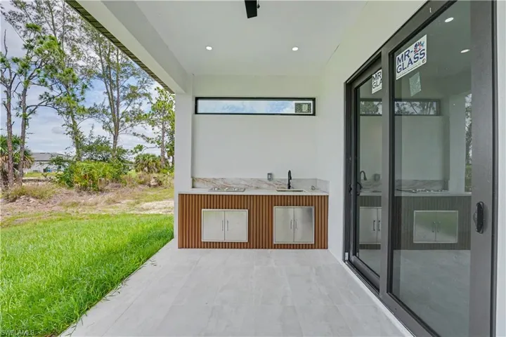 Outdoor kitchen featuring a stone countertop, built-in sink with a matte black faucet, wood-finish slatted cabinetry, and stainless steel under-counter storage