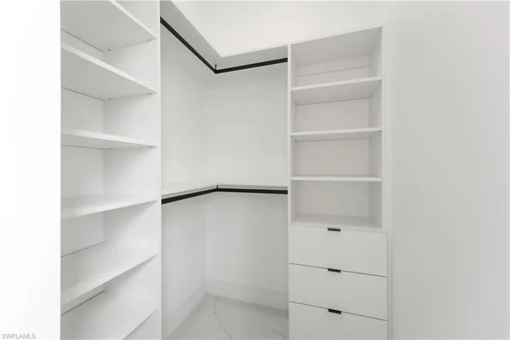 Custom closet system featuring white shelving, multiple drawers with dark hardware, and dark hanging rods