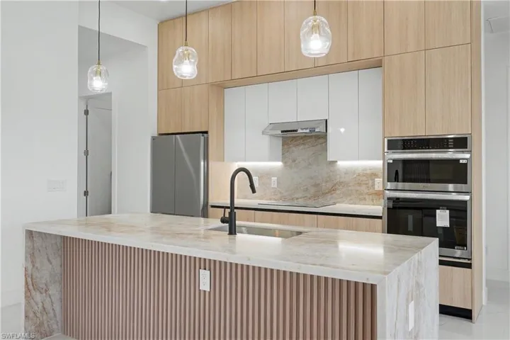 Modern kitchen featuring a waterfall island with stone countertop, stainless steel appliances, wood-finish cabinetry, and contemporary pendant lighting