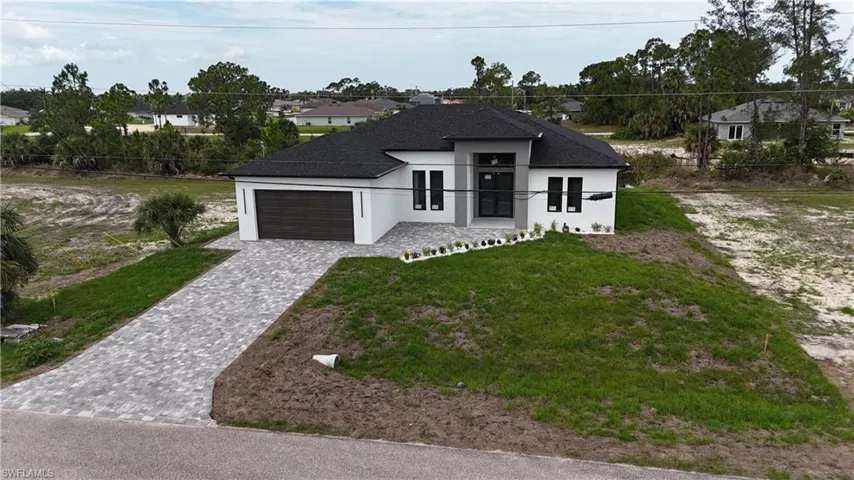 Contemporary architectural style home featuring a dark shingle roof, white exterior siding, a dark wood-finish garage door, and a paver driveway