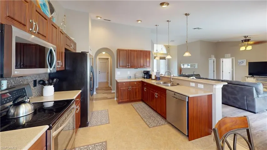Kitchen with ceiling fan, hanging light fixtures, sink, appliances with stainless steel finishes, and a high ceiling