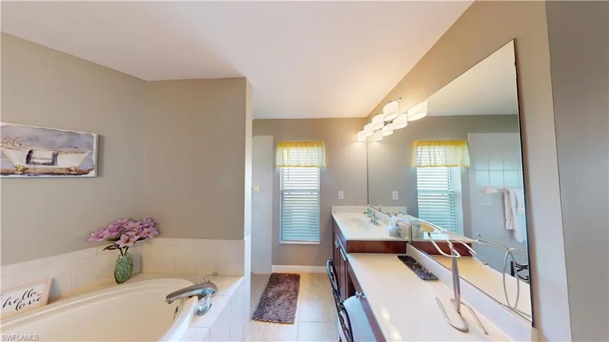 Bathroom featuring tiled tub, vanity, and tile patterned flooring