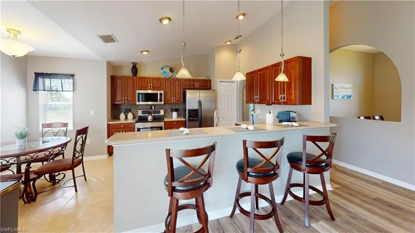 Kitchen featuring kitchen peninsula, hanging light fixtures, light hardwood / wood-style flooring, stainless steel appliances, and high vaulted ceiling