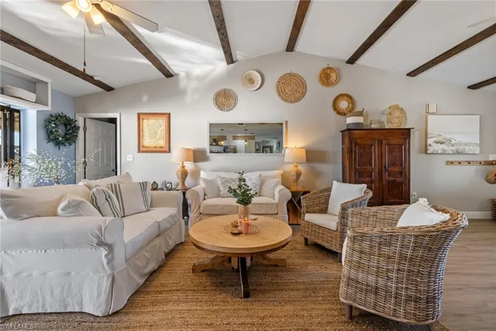 Living room with wood-type flooring, lofted ceiling with beams, and ceiling fan